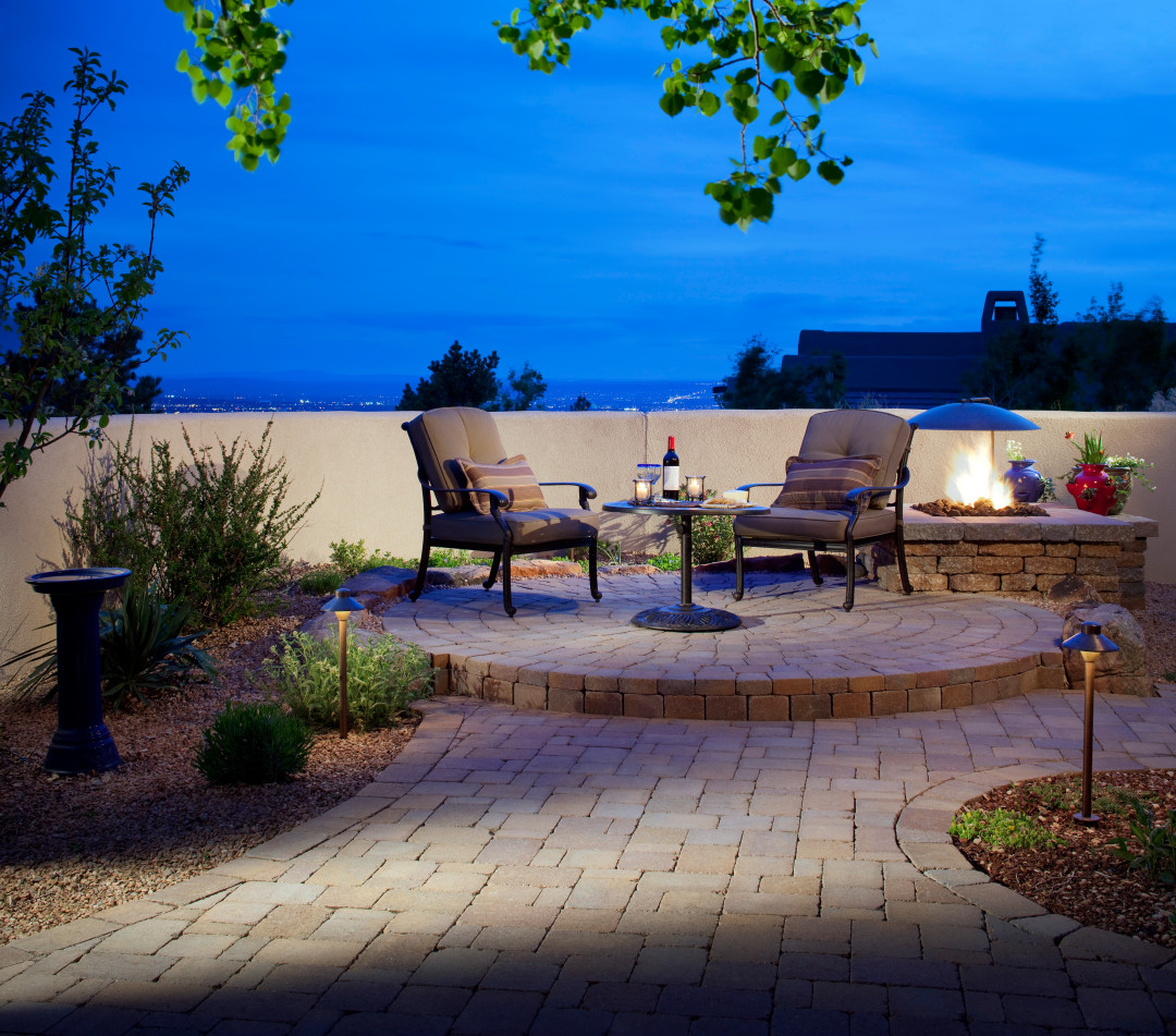 Outdoor living patio with seating, stone pavers, and fire pit designed by Albuquerque landscaping contractors.